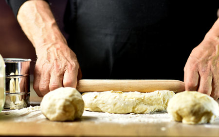 Male hands kneading dough with a rolling pin on a wooden board
