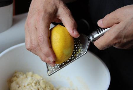 Elderly woman grating lemon on a grater in the kitchen
