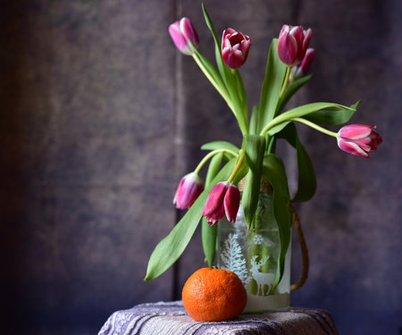 Tulips in a vase and tangerine on a dark backgroundの写真素材