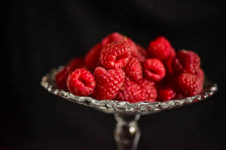 Ripe raspberries in a glass vase on a black background