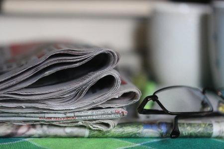 Newspaper and eyeglasses on green tablecloth, stock photo.