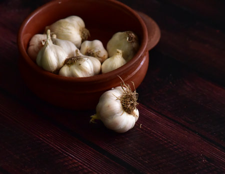 Garlic bulbs in a clay bowl on a dark wooden background.の写真素材