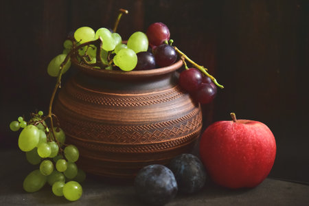 Still life with fresh grapes and apples in clay vase on wooden backgroundの写真素材