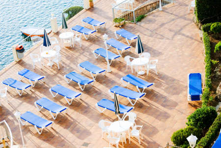a horizontal image of rows of blue sun loungers on a patio in early morning sunshine viewed from a high vantage pointの写真素材