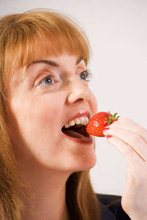 a vertical image of a close up of a pretty young woman taking a bite from a strawberryの写真素材
