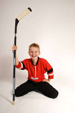 a vertical image of a young boy with his hockey top and kneeling with his hockey stick against a plain backgroundの写真素材