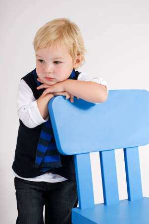 a vertical image of a handsome young boy looking thoughtful and leaning on a blue chairの写真素材