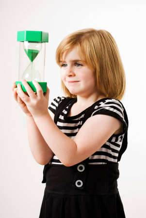 a vertical image of a young girl looking at sand flowing through a hourglass