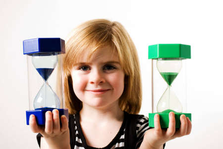 a horizontal image of a young girl holding up two hourglassesの写真素材