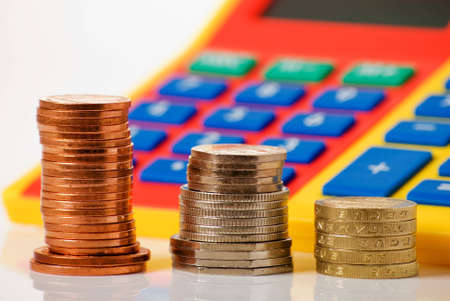 a horizontal image of a brightly coloured calculator and stacks of coins, focus on coinsの写真素材