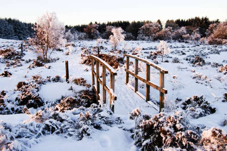 a horizontal image of a winter countryside setting with the sun setting on a wooden bridgeの写真素材
