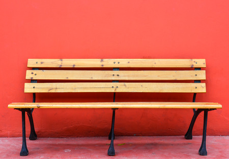 wooden long bench against blank red wall on backgroundの写真素材
