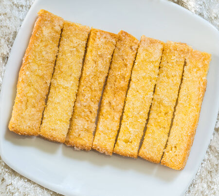 Baked bread buttered and sprinkled with sugar granules in white dish