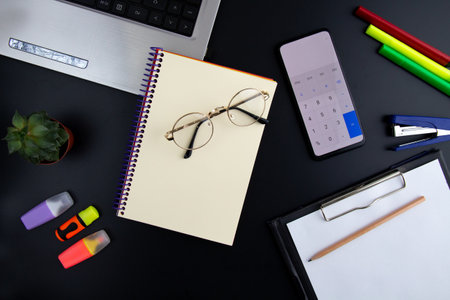 computer, calculator, notepad, papers and colored pencils on black background