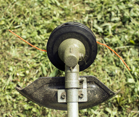 A top part of a brush cutter, behind is a blurred grass.