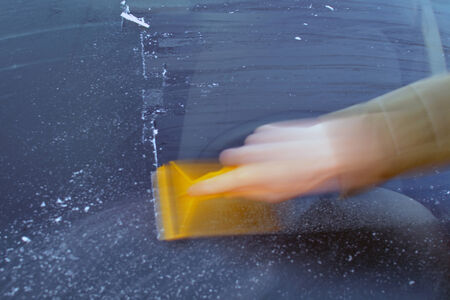 Removing ice from a car windshield in the morning.の写真素材