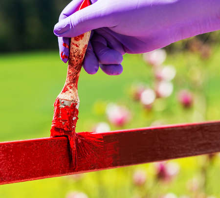 Hand wearing purple gloves and painting with a paint brush.