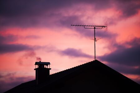 Morning scene with a house silhouette, chimney and tv antenna.の写真素材