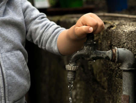 Hand from a child is turning tap water valve and letting water out.