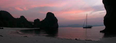 A sailboat anchored offhore near a beach in Thailand at sunset.の写真素材