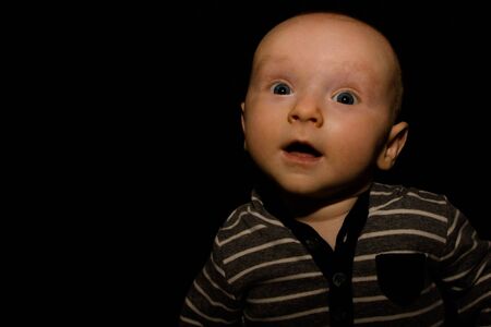 A 4 Month Old Baby Poses on a Black Background. Perfect for Memes with Copy Space.