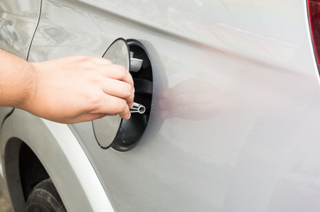 A man operning a cover of the fuel tank of a silver carの写真素材