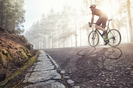 Cyclist on road in a foggy forestの写真素材