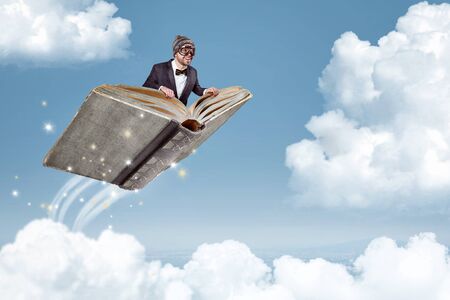 Man flying on a book over the cloudsの写真素材