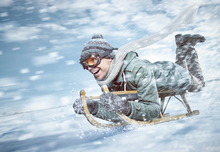 Cheerful man sledding down a snowy slope in full speed