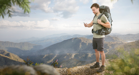 Hiker with a smartphone standing in front of a tropical mountain panoramaの写真素材