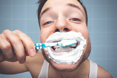 Funny portrait of a man brushing his teeth with a lot of foam