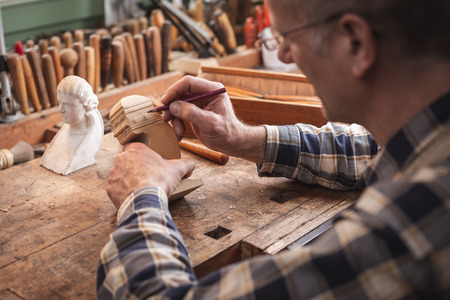 Mature artisan sketching the outlines of a sculpture with a pencilの写真素材