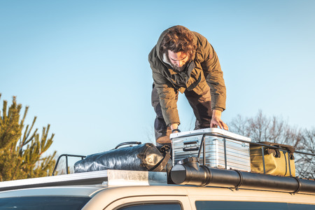 A bearded man is checking the luggage stored on the roof of his camper vanの写真素材