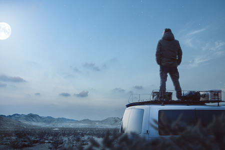 Young man enjoying a moonlit night on top of his camper vanの写真素材