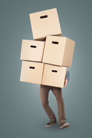 A man is carrying a overwhelming stack of cardboard boxes in his armsの写真素材