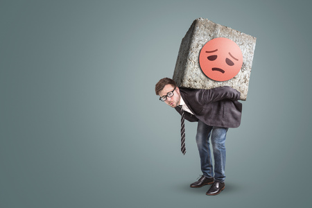 Unhappy entrepreneur bending under a large stone on his backの写真素材