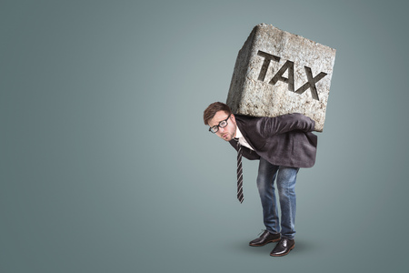Businessman bending under a heavy stone with the word TAX printed on itの写真素材