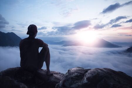 Young man enjoying the sunrise on a mountain peak above the clouds