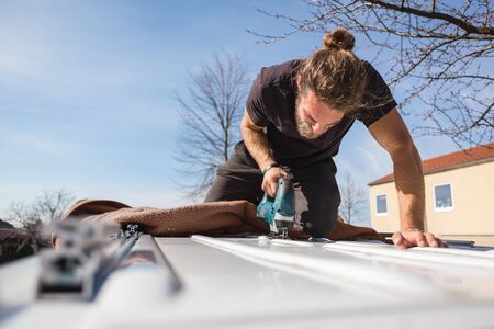 Man using a jigsaw to saw into the roof of a vanの写真素材
