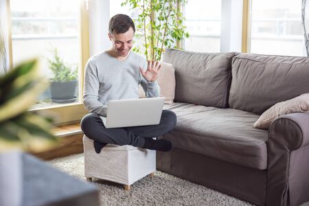 Man at home waving at the laptop screenの写真素材