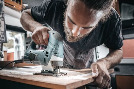 Young man working with a jigsaw inside a camper vanの写真素材