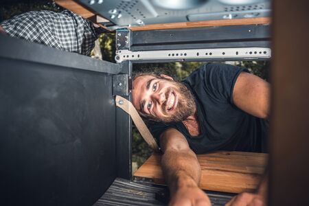 Man smiling while working on a cupboard in his camper vanの写真素材