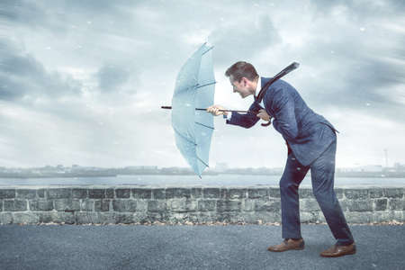Businessman with an umbrella is facing strong headwindの写真素材