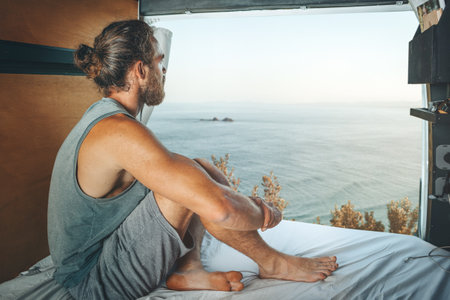 Man sitting in the back of a camper van looking at the seaの写真素材