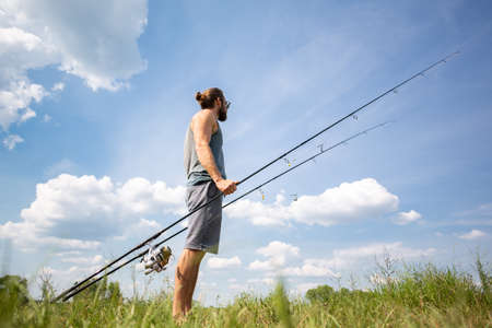 Young man carrying two carp fishing rodsの写真素材