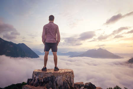 Man standing on a mountain top above the clouds