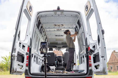 Man inside a van recording himself with a smartphone on a tripod