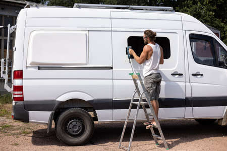 Camper van conversion - Man cut a hole for a window into the side doorの写真素材
