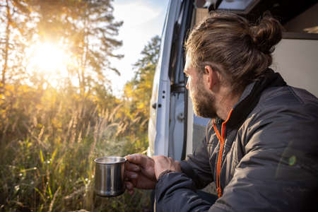 Man having a morning coffee in the doorway of his camper van in autumnの写真素材