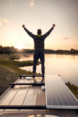 Man enjoying his freedom on top of a camper van at sunsetの写真素材